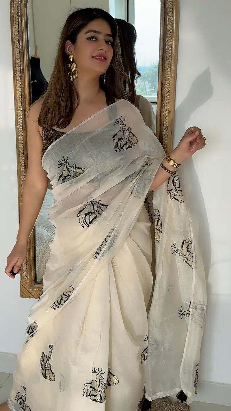 Woman wearing a white saree with black patterns in a room.
