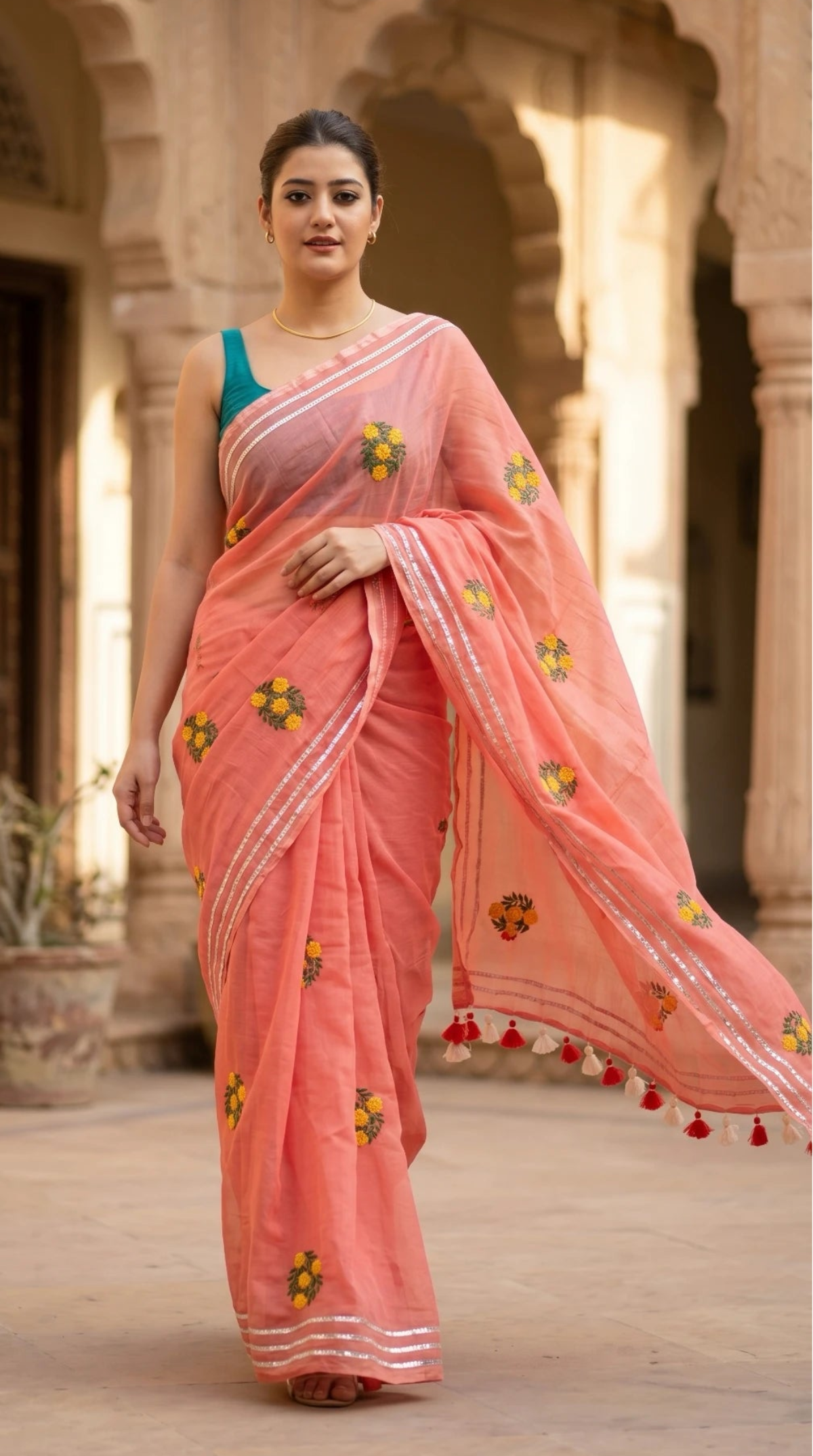 Woman in a pink saree with floral patterns standing in an architectural setting.