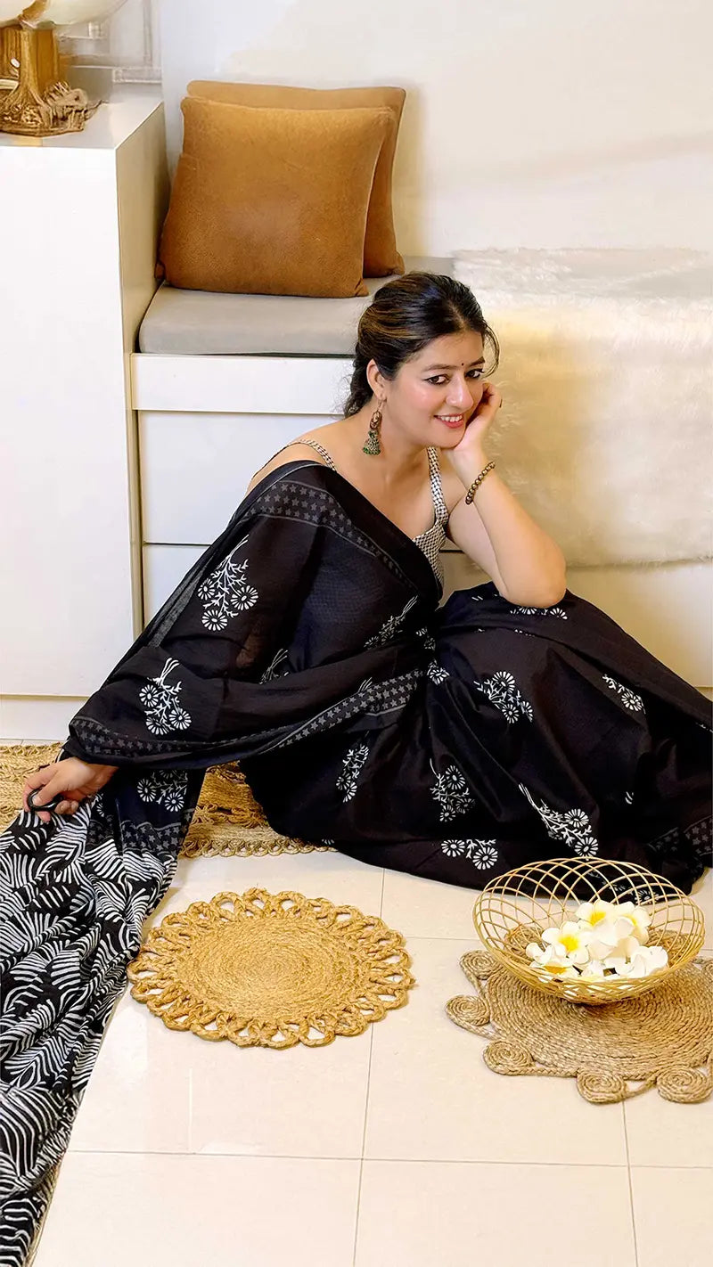 Woman in a black saree with white patterns sitting on a couch in a living room.