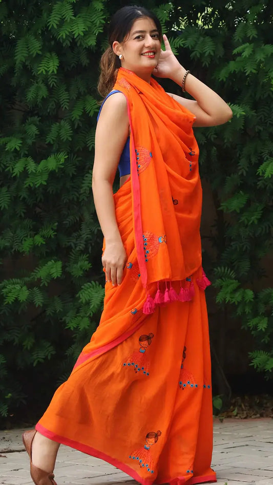 Woman wearing an orange saree with a green foliage background
