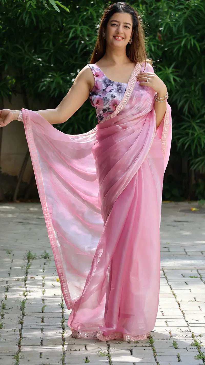 Woman wearing a pink saree with a floral blouse against a green outdoor background