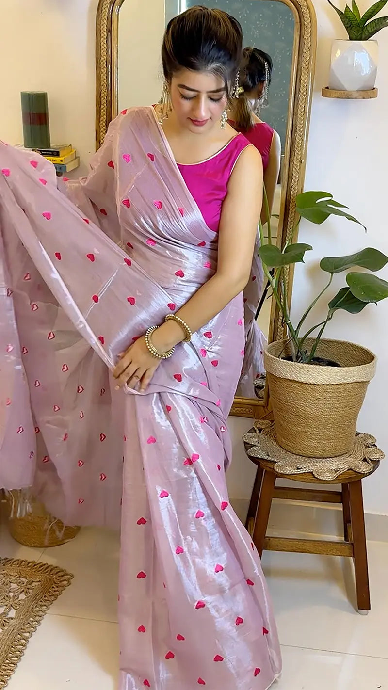 Woman in a pink saree with heart patterns standing in front of a mirror.