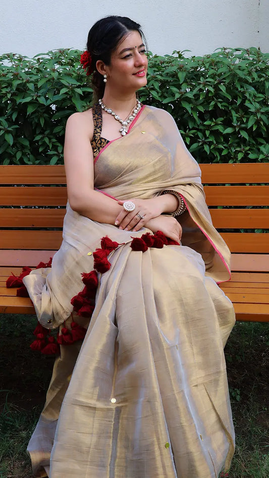 Woman in a gold saree with ginni chumki sitting on a bench outdoors.