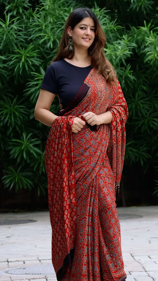 Woman wearing a red and black patterned saree with a green leafy background