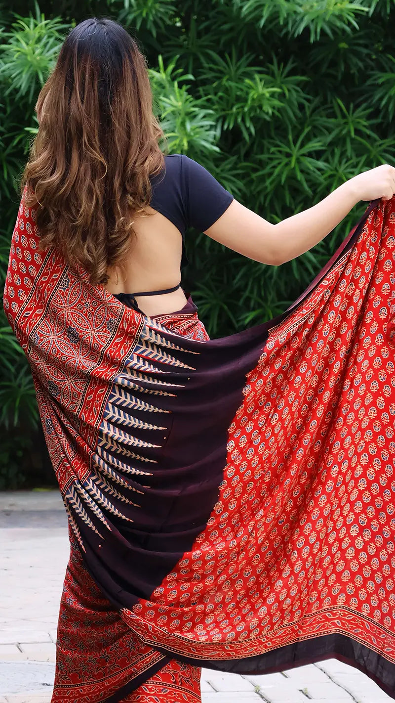 Woman wearing a red and black patterned saree with a green leafy background