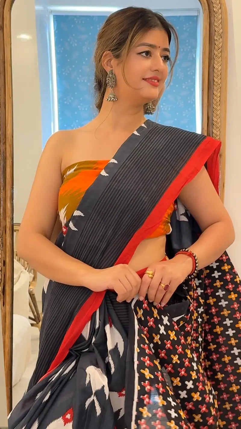 Woman wearing a saree with a colorful pattern, standing in front of a mirror.