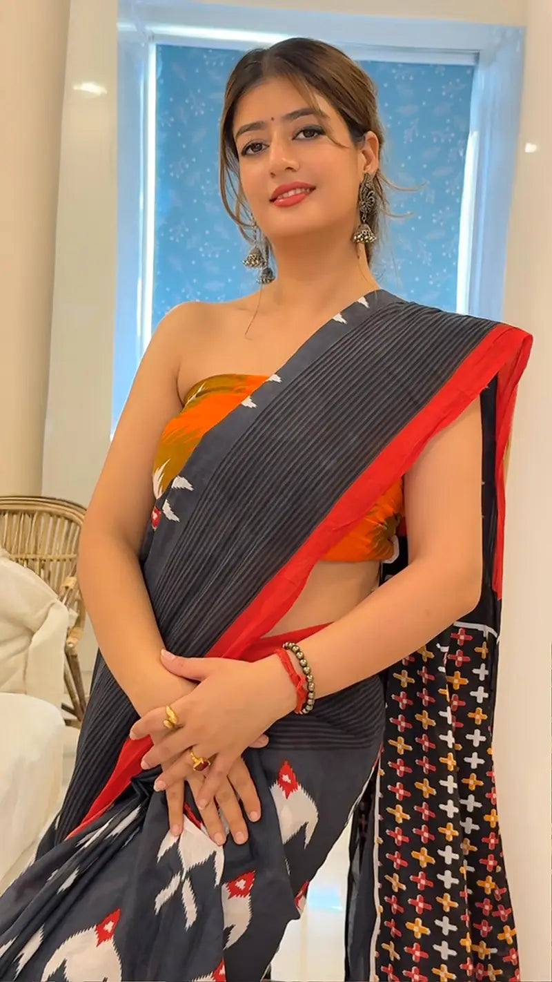Woman wearing a saree with a colorful blouse, standing indoors.