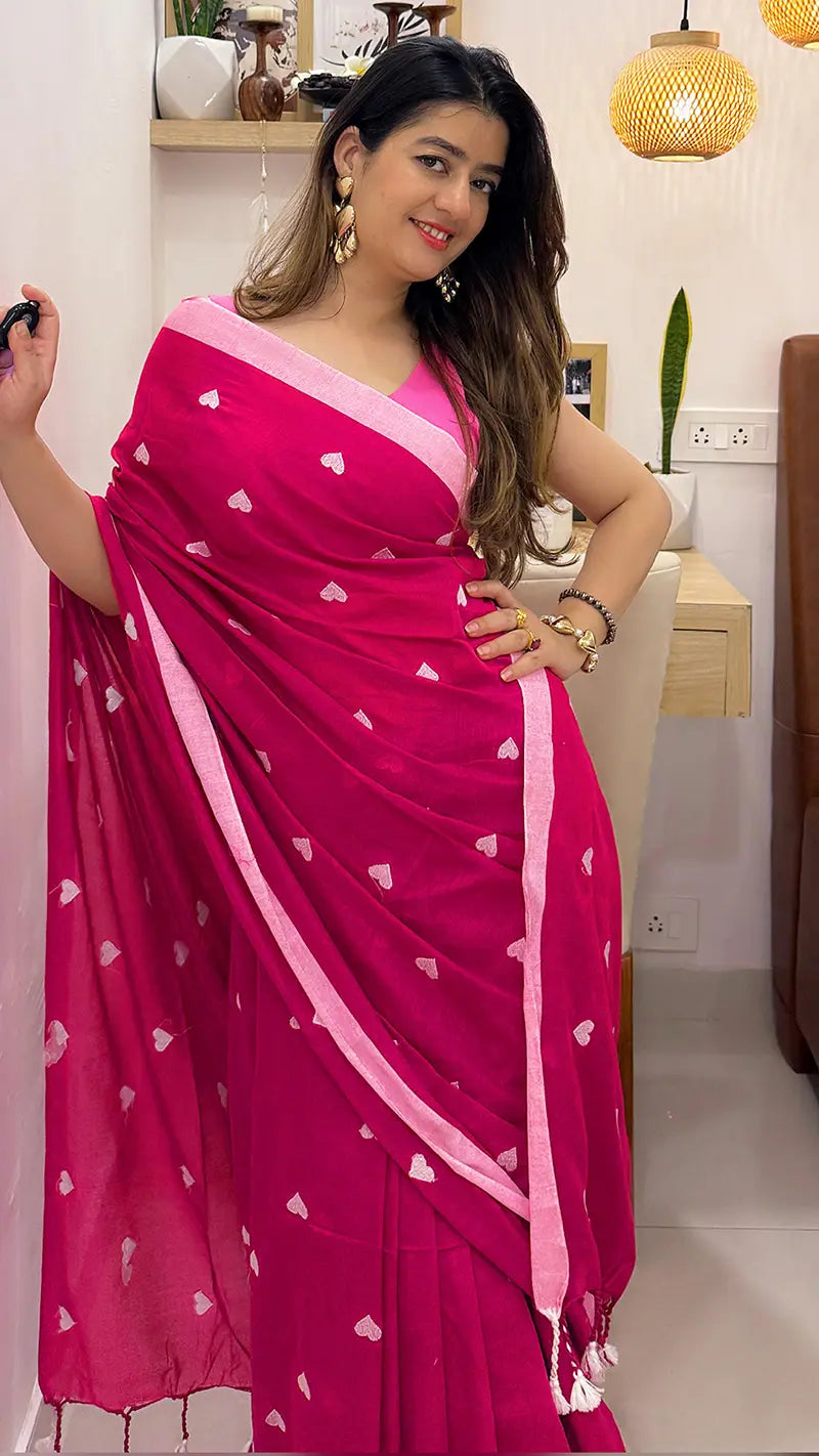 Woman wearing a pink soft cotton saree with heart patterns indoors.