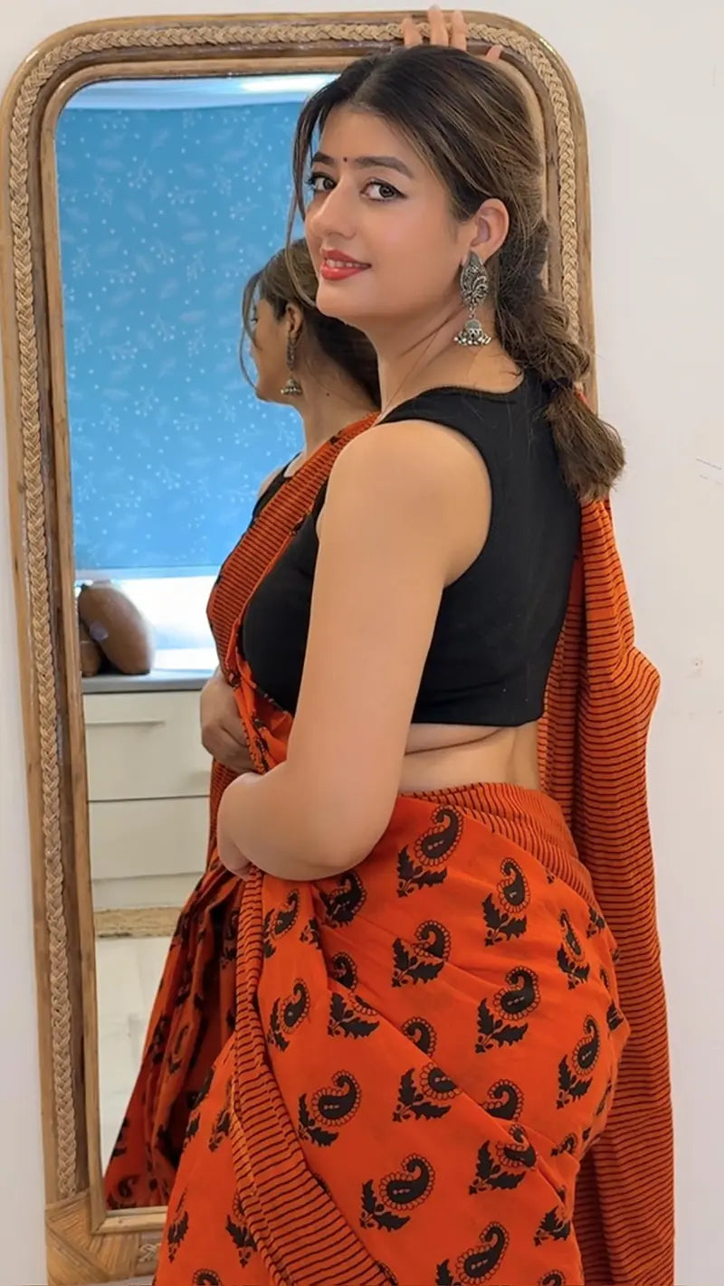 Woman in black top and orange patterned skirt standing in front of a mirror.