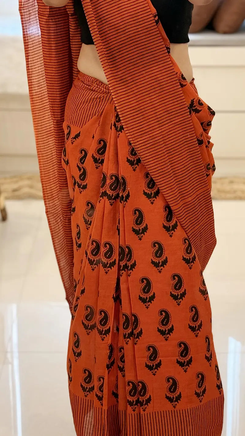 Orange traditional saree with black patterns on a neutral background