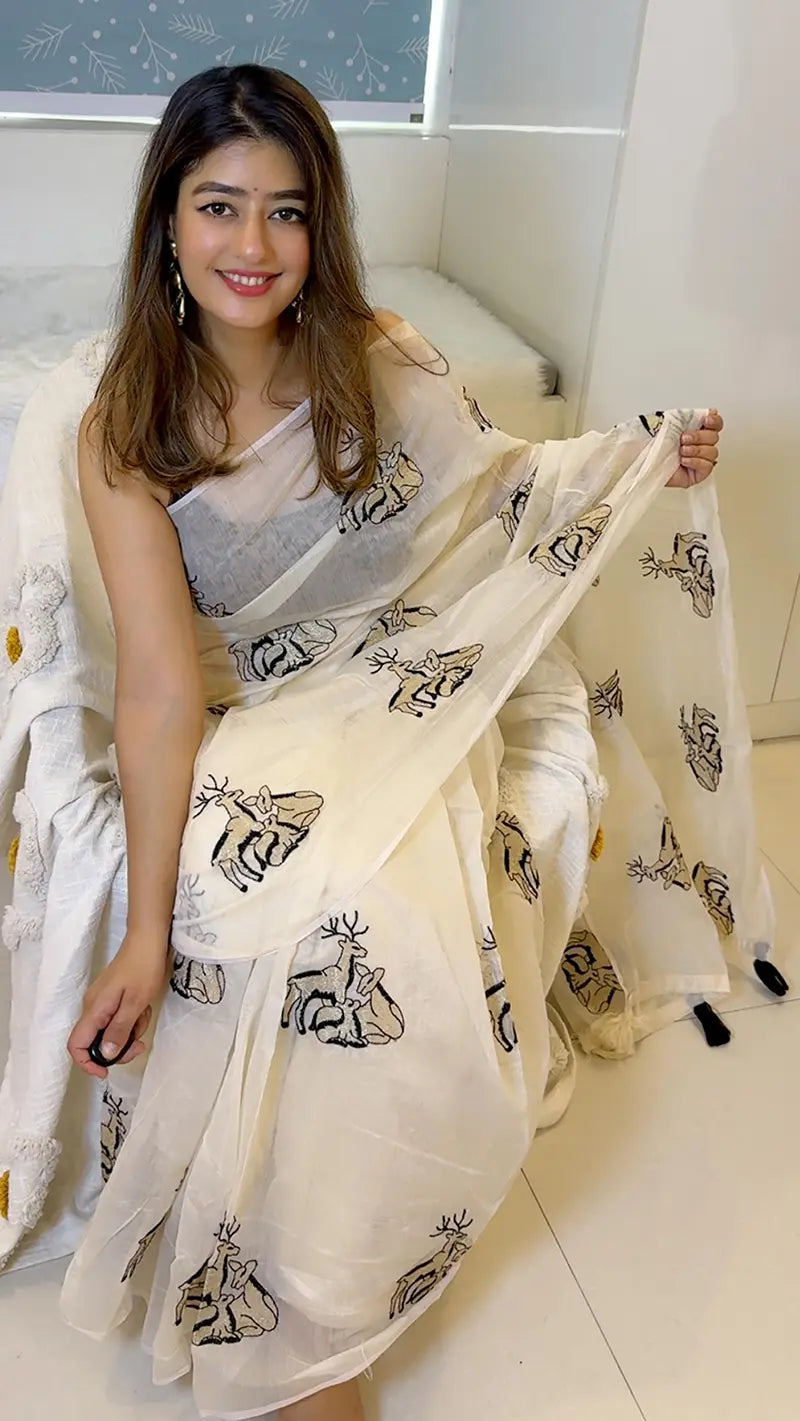 Woman holding a white saree with black patterns in a room.
