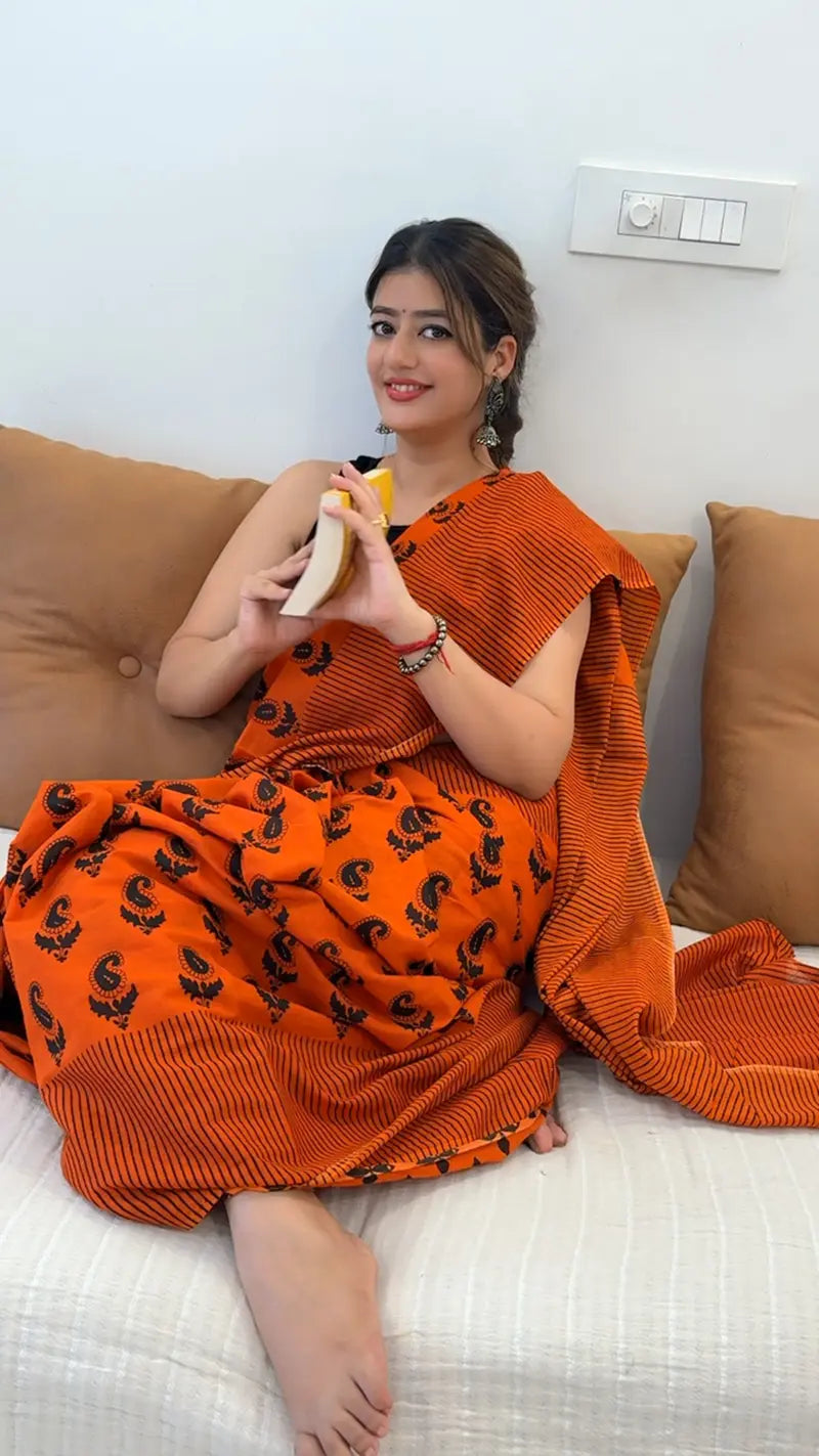 Woman in an orange saree sitting on a couch holding a banana.