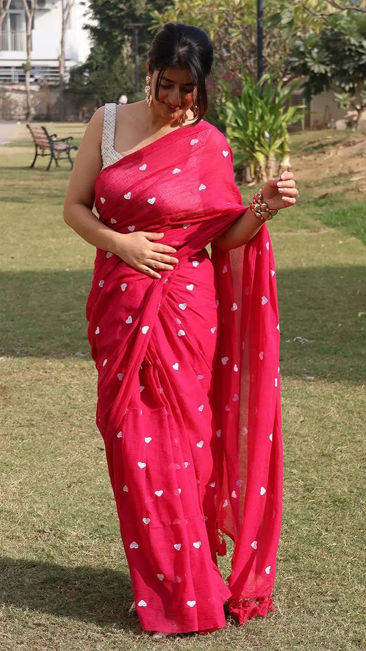 Woman in a pink mul cotton saree with white heart embroidery standing outdoors on grass