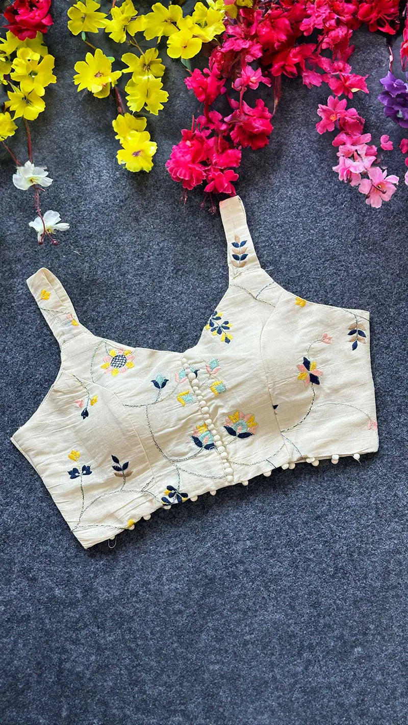 Beige blouse with floral embroidery on a dark surface with colorful flowers around