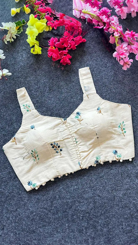 Embroidered beige blouse with floral patterns on a dark surface with flowers in the background