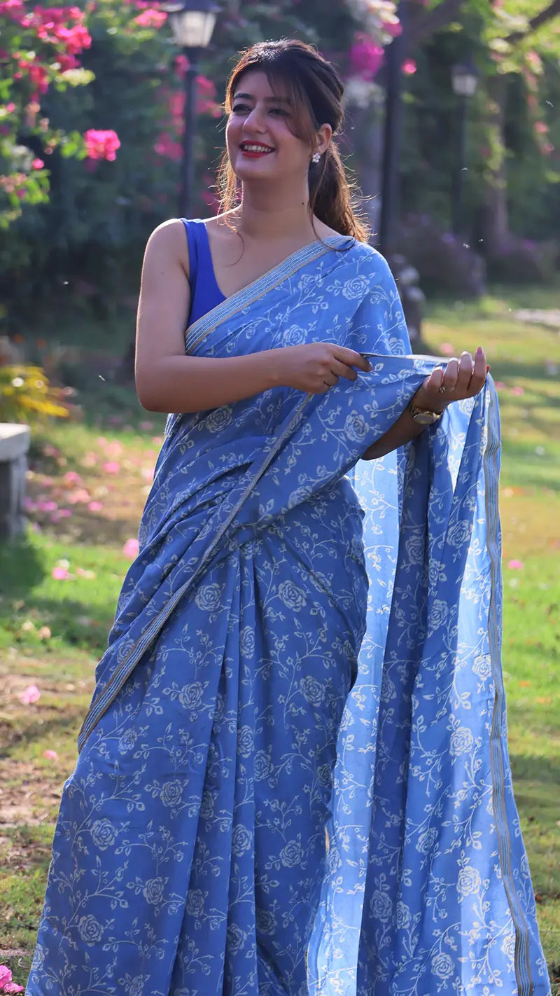 Woman in a blue muslin print saree standing outdoors with greenery in the background