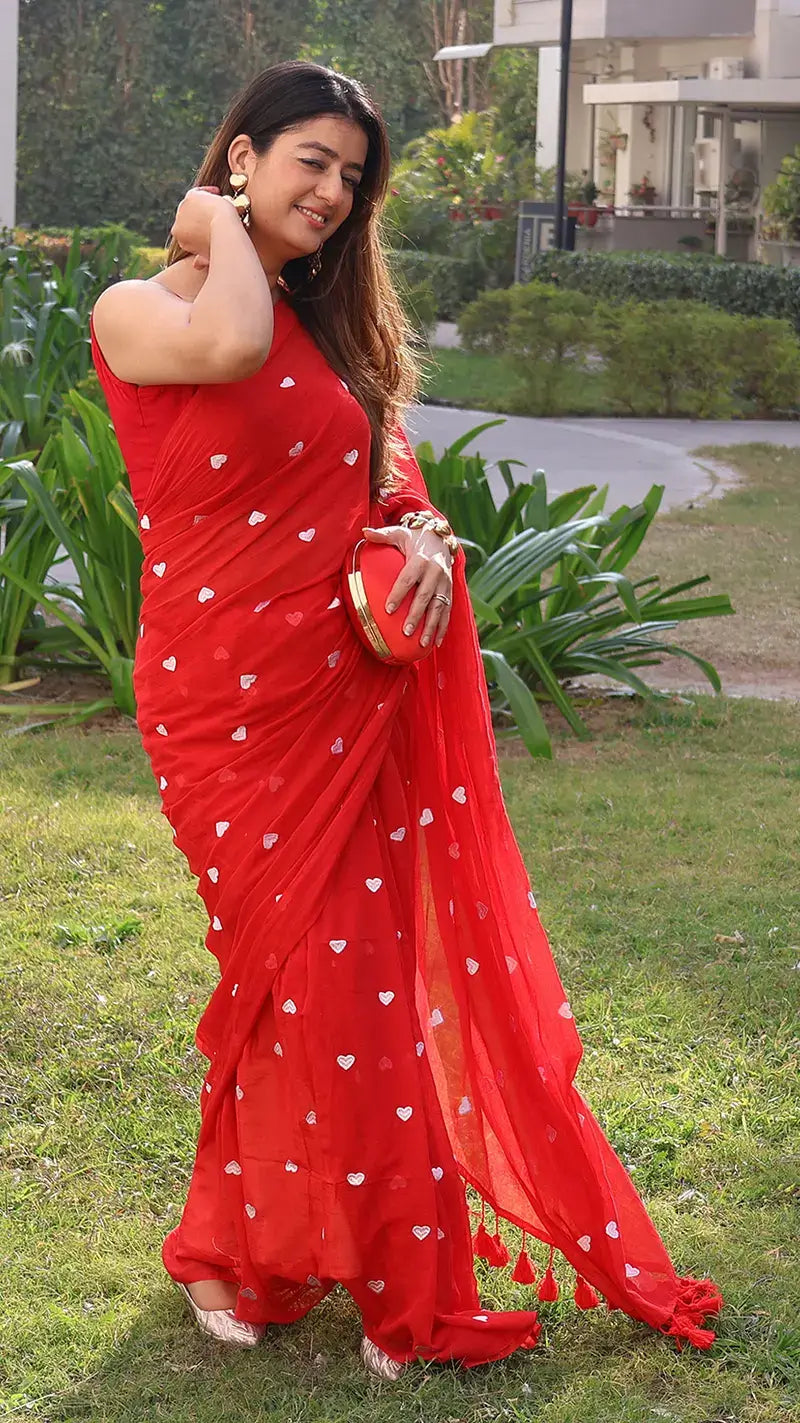 Woman wearing a red mul cotton saree with white embroidered hearts outdoors.