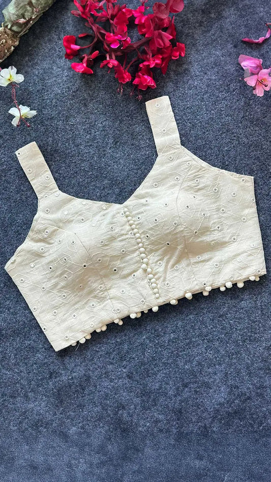 Beige blouse with floral embroidery on a dark textured surface with flowers.