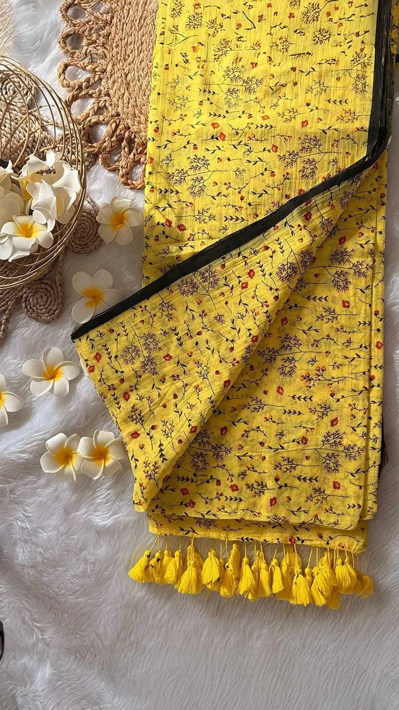 Yellow saree with floral patterns and tassels on a textured surface with flowers.