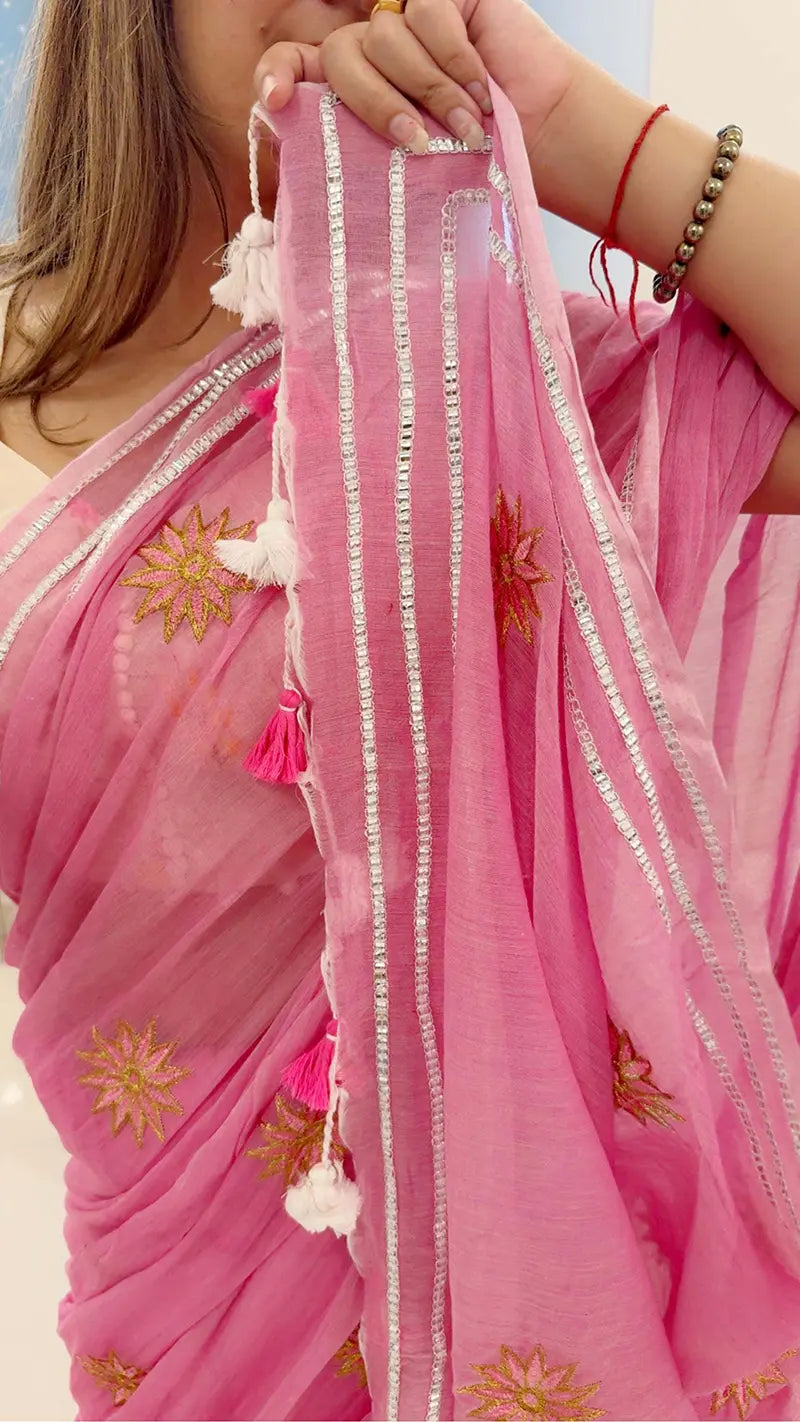 Close-up of a pink saree with gold embroidery and tassels, held by a person.