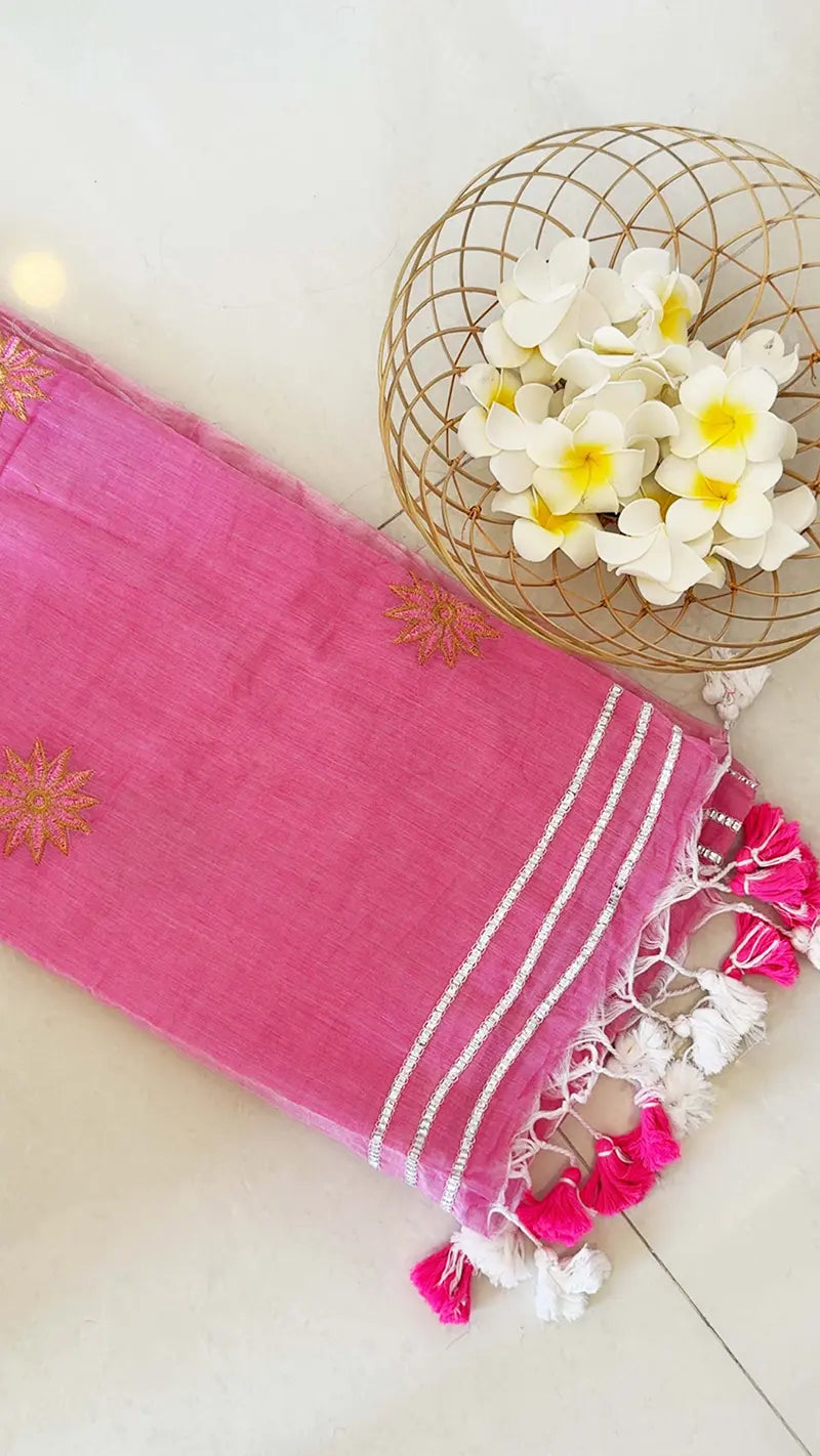 Pink saree with white patterns and tassels on a light surface with decorative elements.