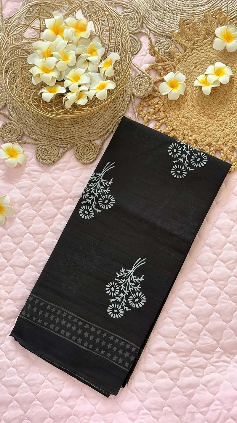 Black saree with white floral embroidery on a pink textured surface with flowers.