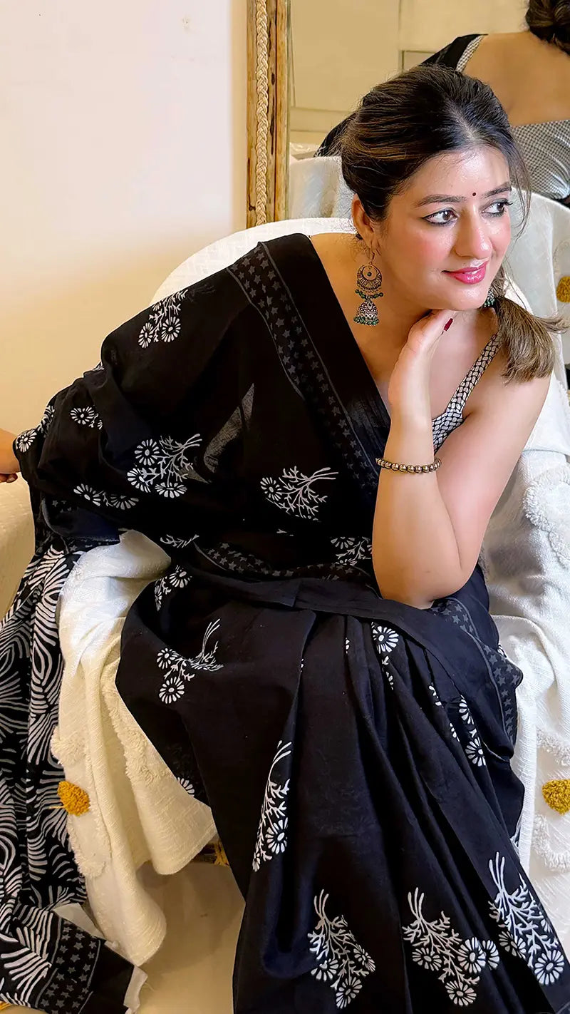 Woman wearing a black saree with white patterns sitting on a couch.