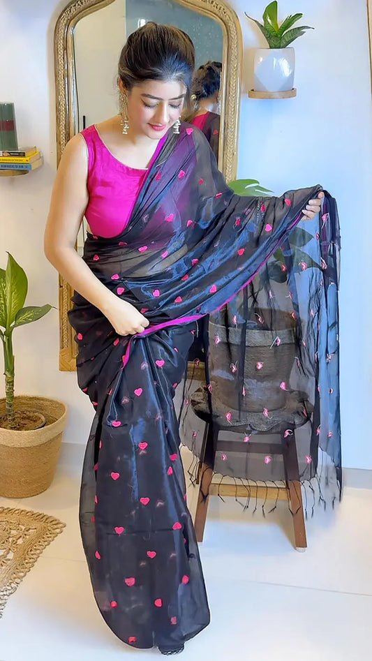 Woman wearing a black saree with pink heart patterns in front of a mirror