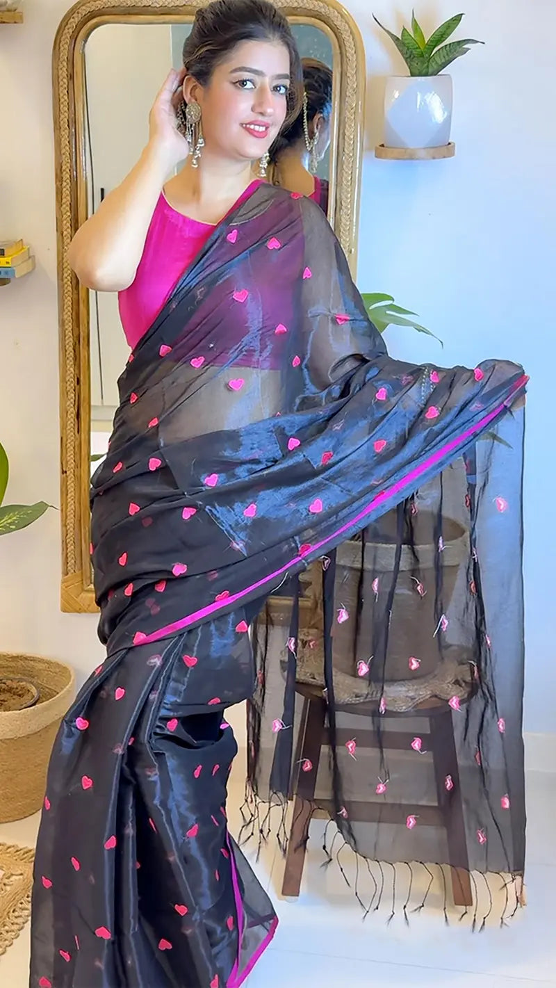 Woman wearing a black saree with pink embroidered hearts in front of a mirror.