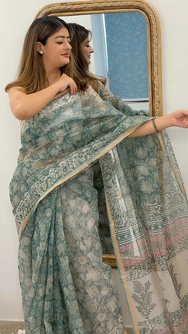 Woman wearing a green floral saree in front of a mirror.