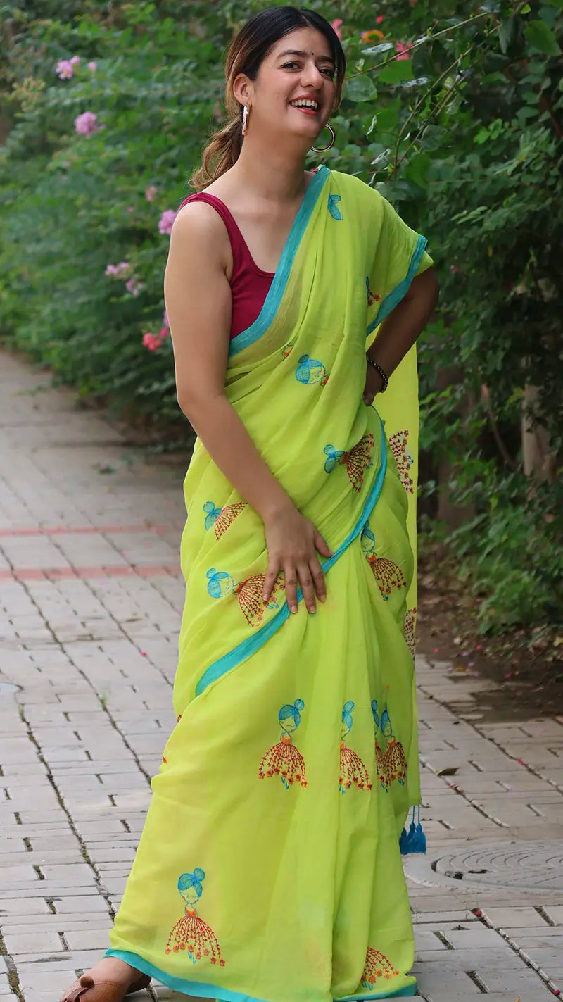 Woman wearing a bright green mul cotton saree with a red blouse in an outdoor setting.