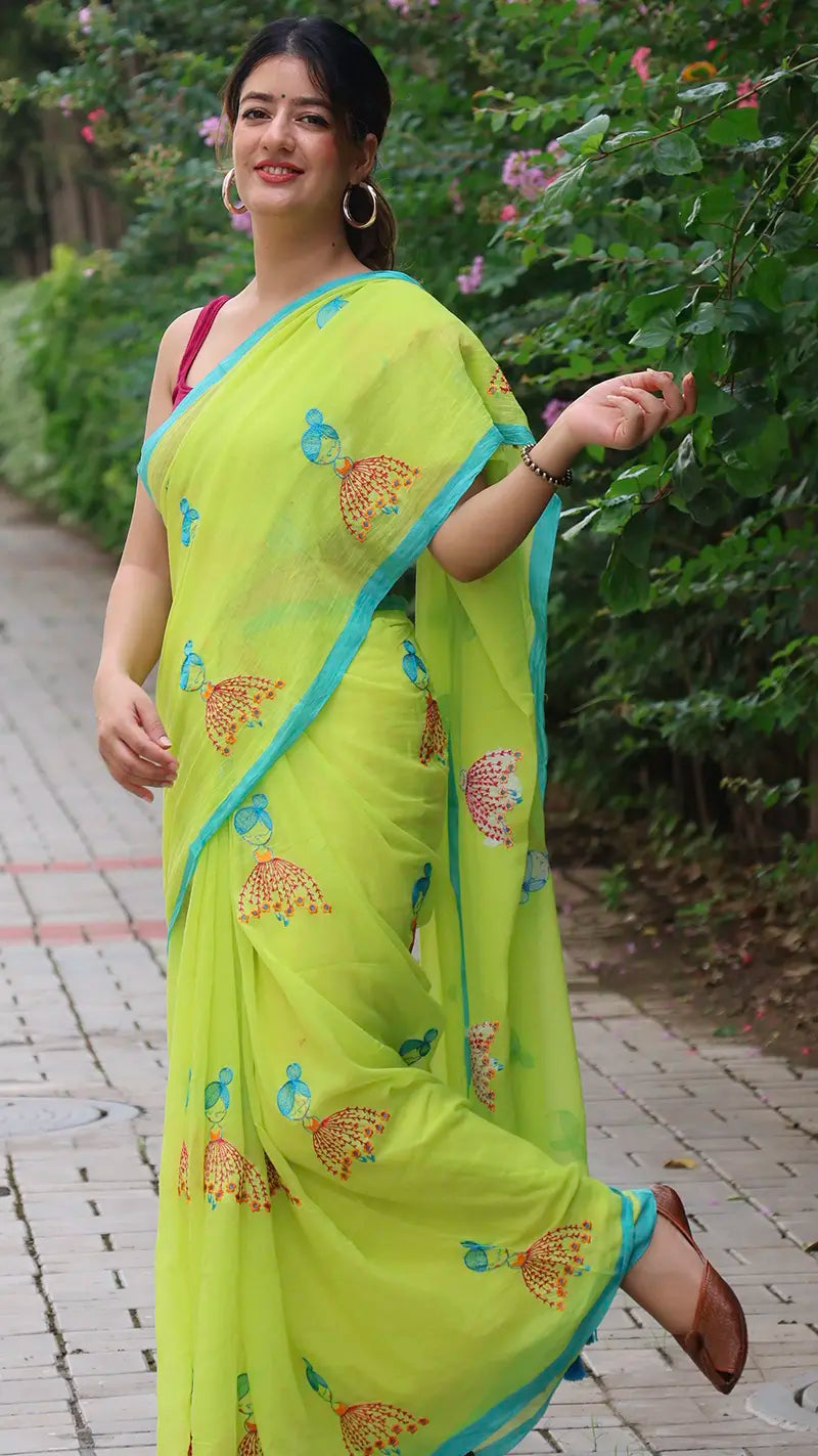 Woman wearing a bright green mul cotton saree with blue border outdoors.