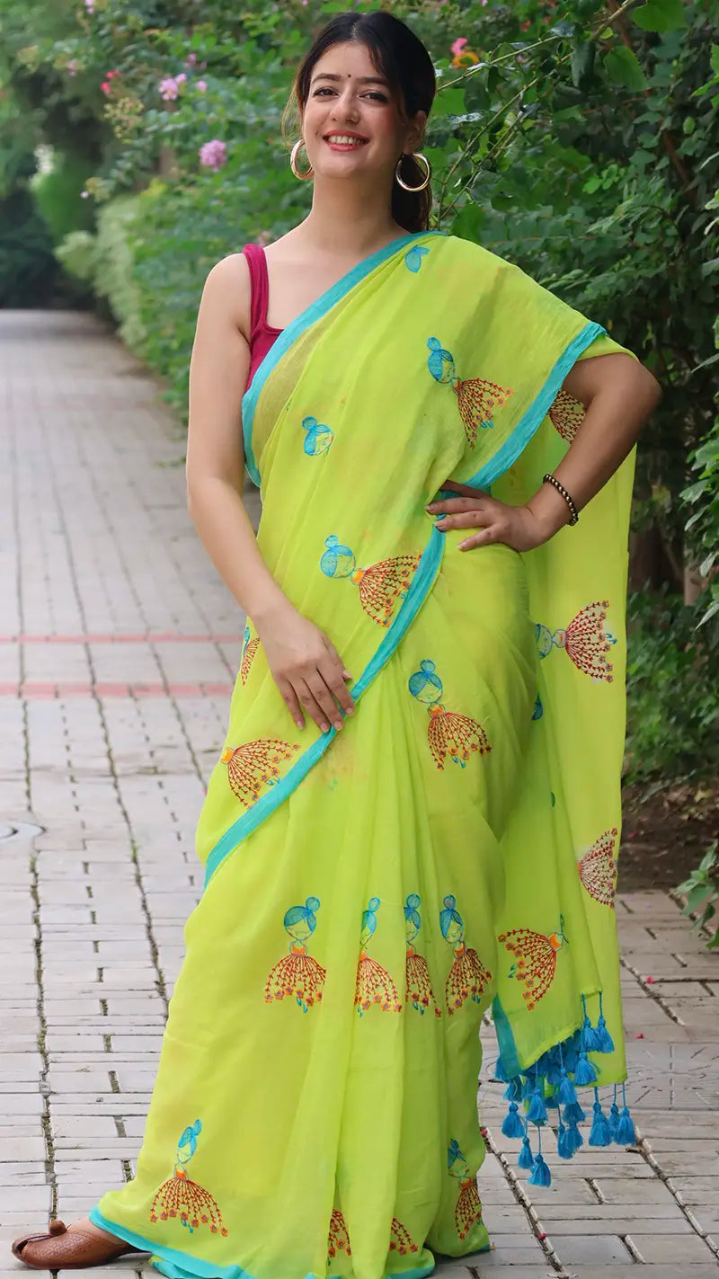 Woman wearing a bright green embroidered mul cotton saree, standing outdoors on a path.
