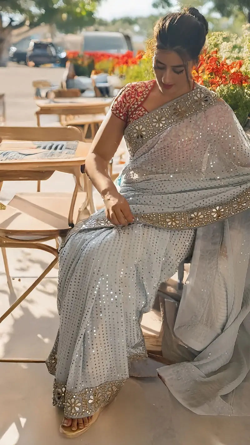 Woman in a Sequin Georgette Saree With Heavy Mirror Work Border with floral blouse sitting outdoors.