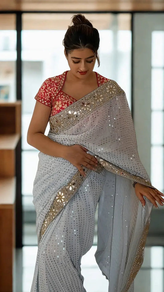 Woman wearing a Sequin Georgette Saree With Heavy Mirror Work Border with a red blouse in an indoor setting