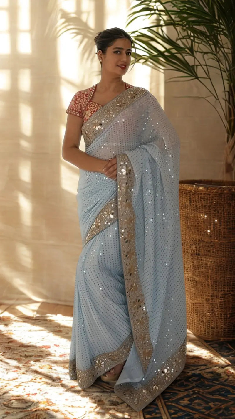 Woman wearing a Sequin Georgette Saree With Heavy Mirror Work Border in a sunlit room.
