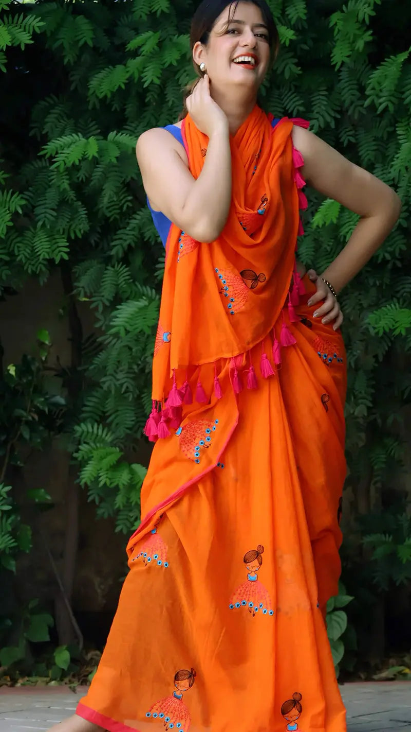 Woman wearing an embroidered orange mul cotton saree with a green leafy background