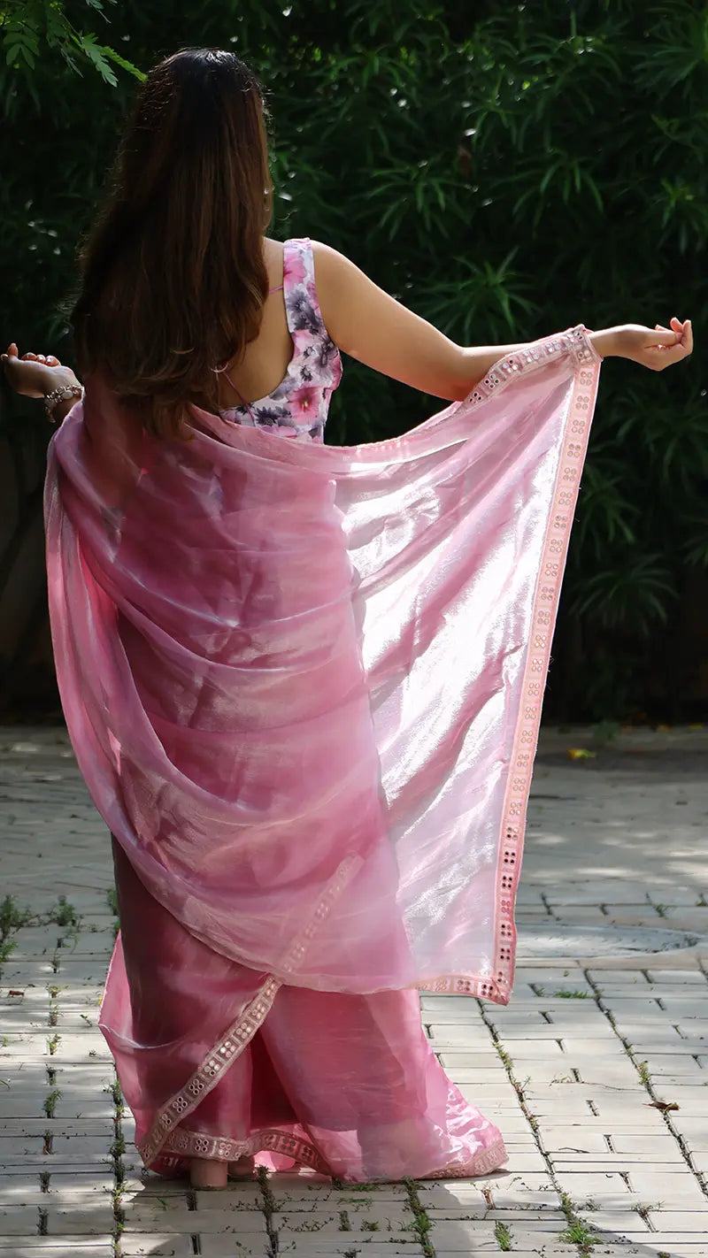 Woman wearing a pink saree with a floral blouse, standing outdoors on a paved path.