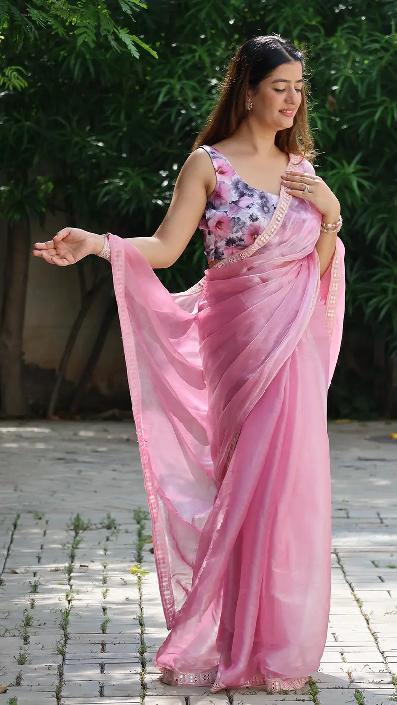 Woman in a pink saree with floral blouse standing outdoors on a paved path.