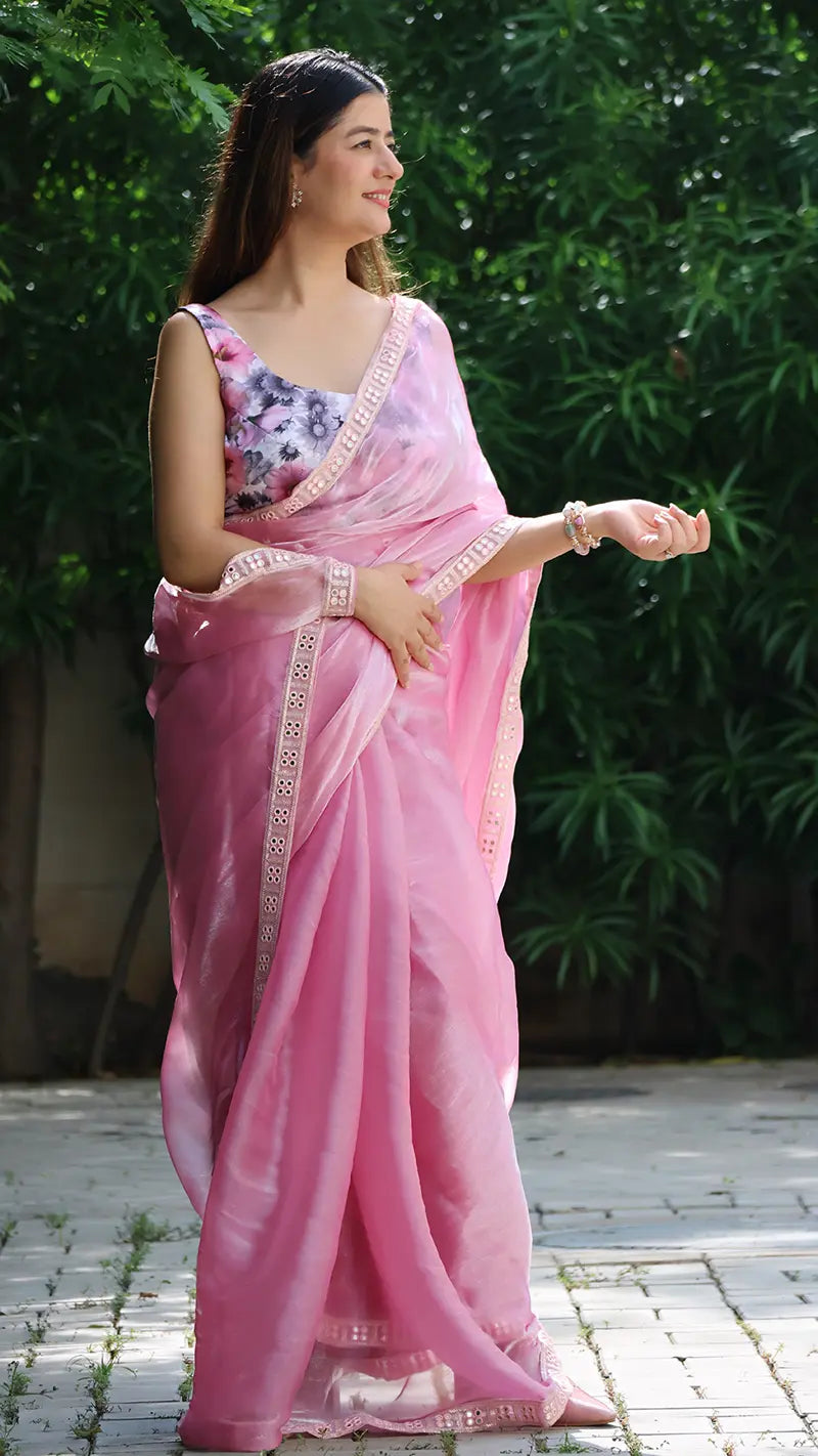 Woman in a pink saree with a floral blouse against a green leafy background