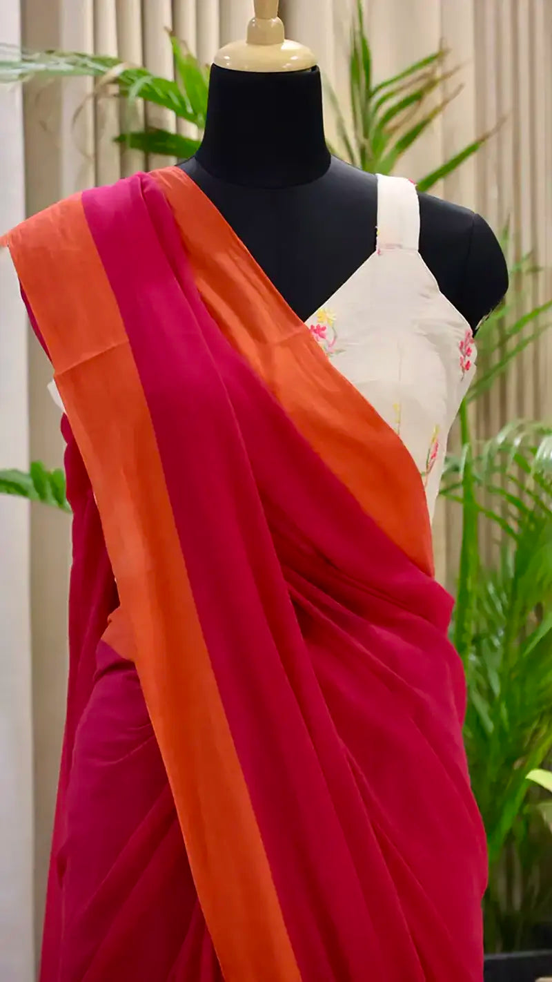 Mannequin wearing a red and orange saree with a white blouse against a green plant background