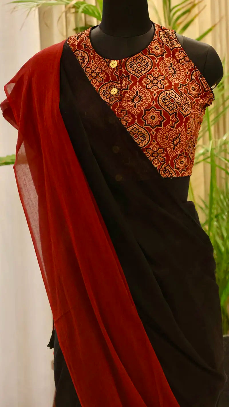 Black saree with a red blouse and red dupatta on a mannequin against a blurred green background