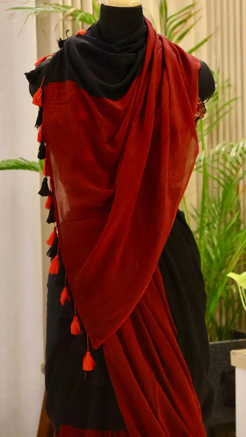 Red and black saree with tassels on a mannequin against a plant-filled background