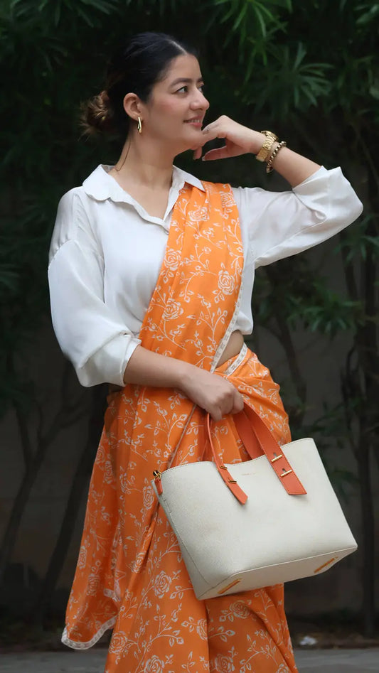 Woman in an orange floral dress holding a white handbag against a dark background