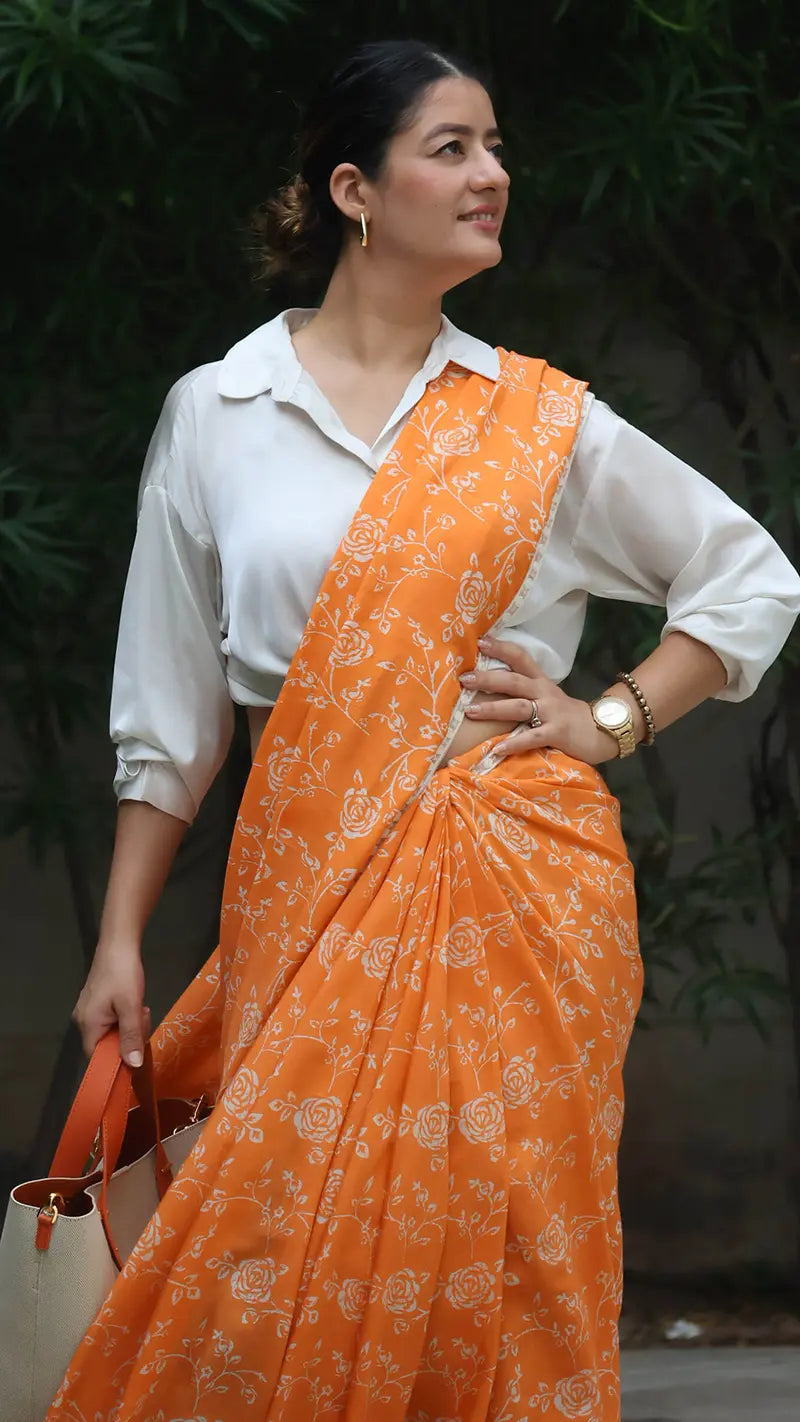 Woman wearing an orange saree with a white blouse against a green leafy background