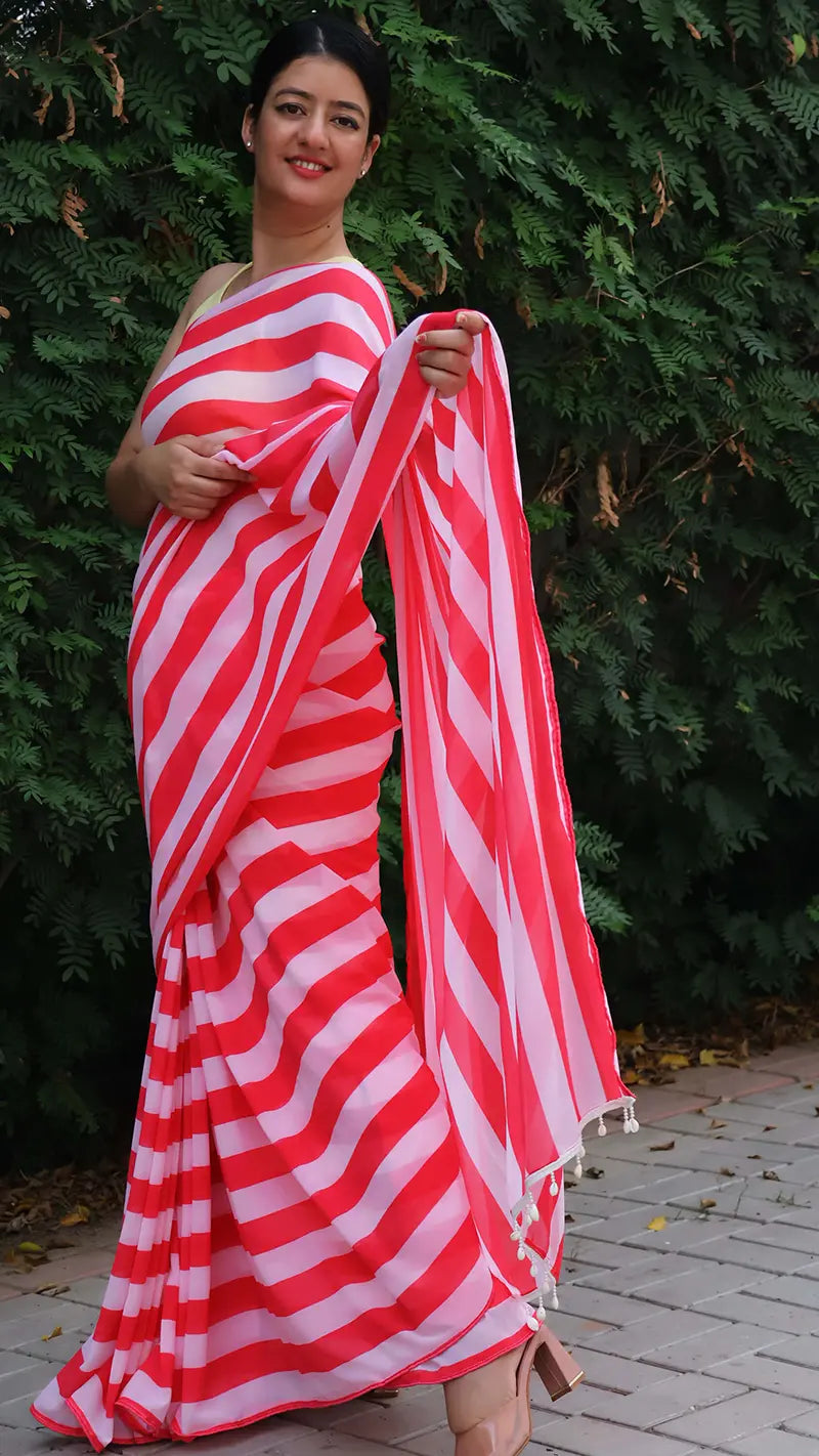 Woman wearing a red and white striped saree standing against a green leafy background.