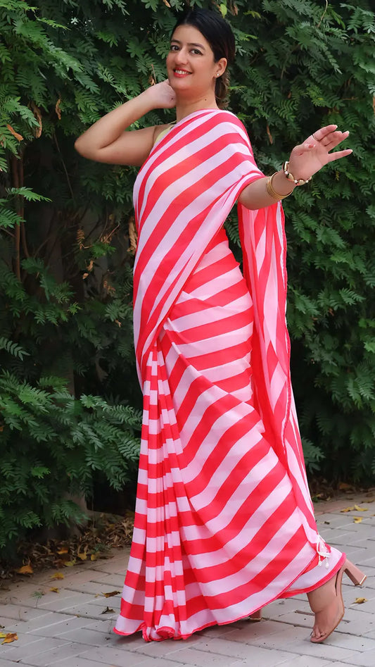 Woman wearing a red and white striped saree standing outdoors with greenery in the background