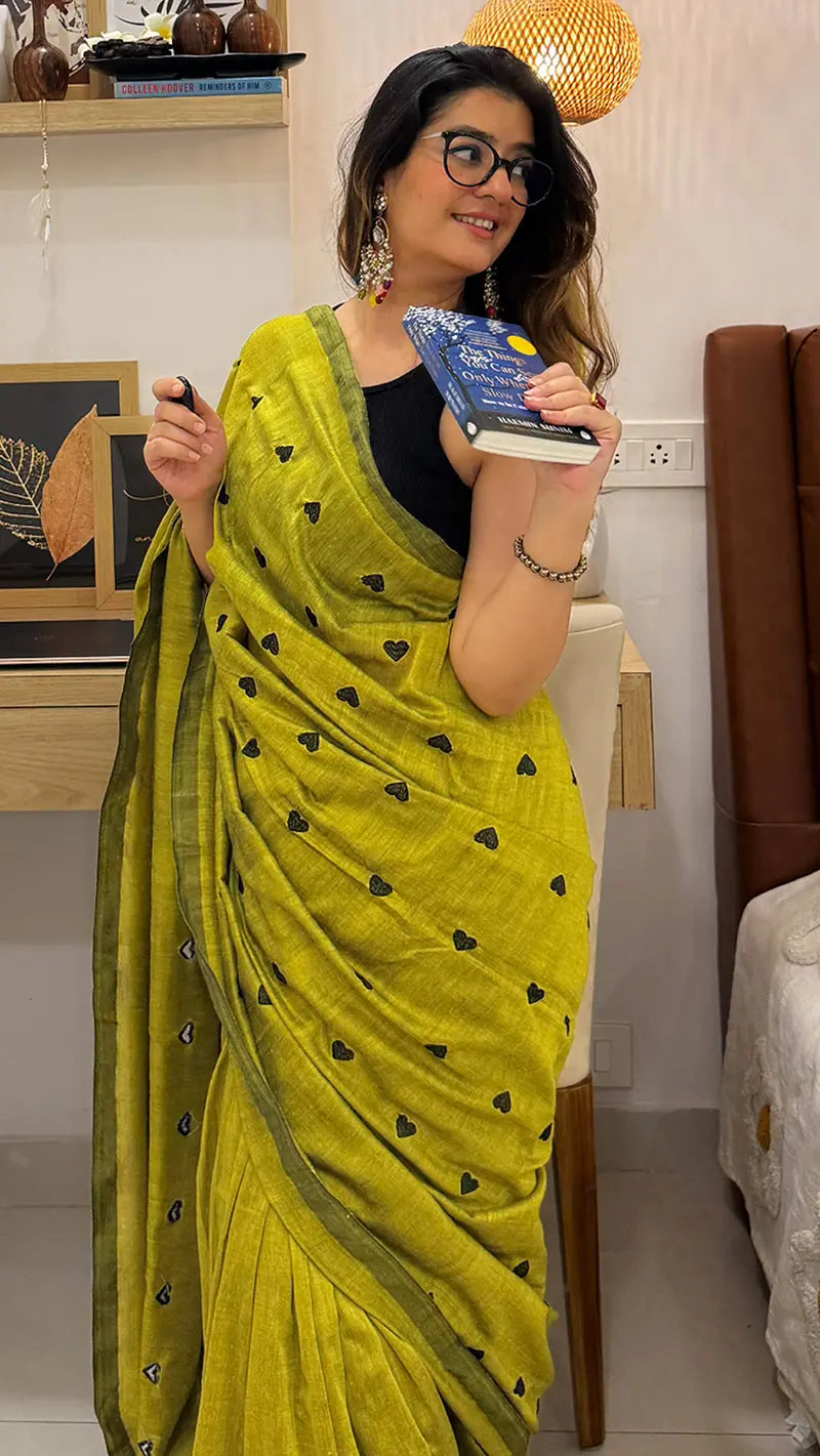 Woman in a soft cotton saree holding a book in a room.