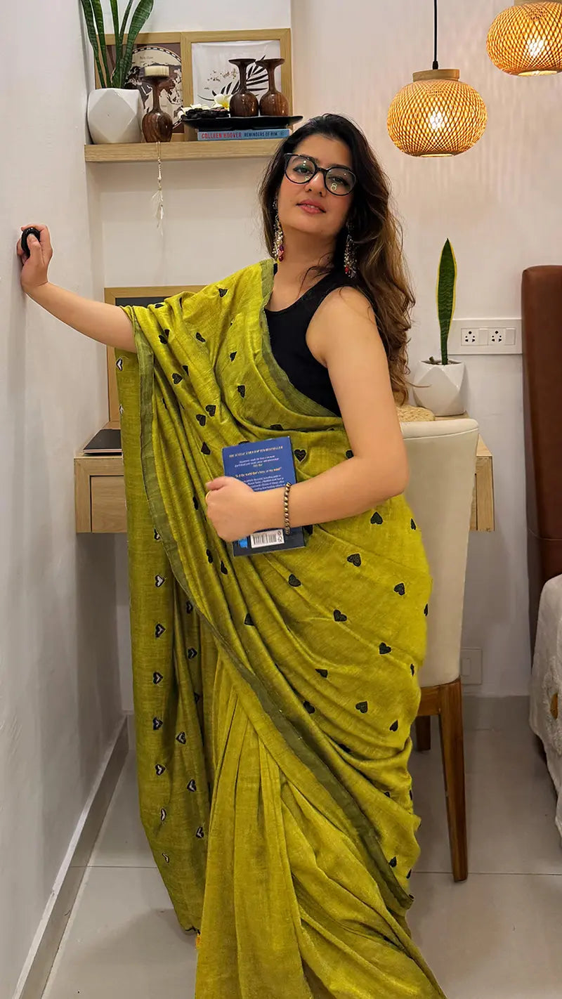 Woman in a green soft cotton saree with black heart embroidery.