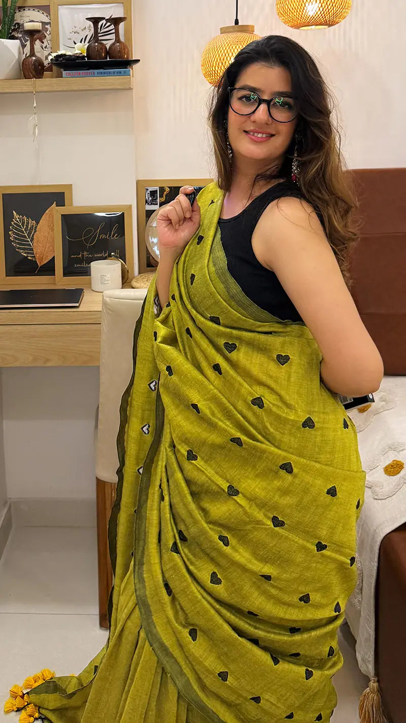 Woman wearing a green soft cotton saree with black heart embroidery in an indoor setting.